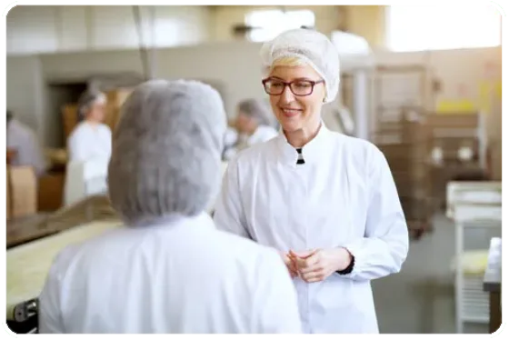 Two workers in the food and beverage industry wearing hairnets engaged in conversation